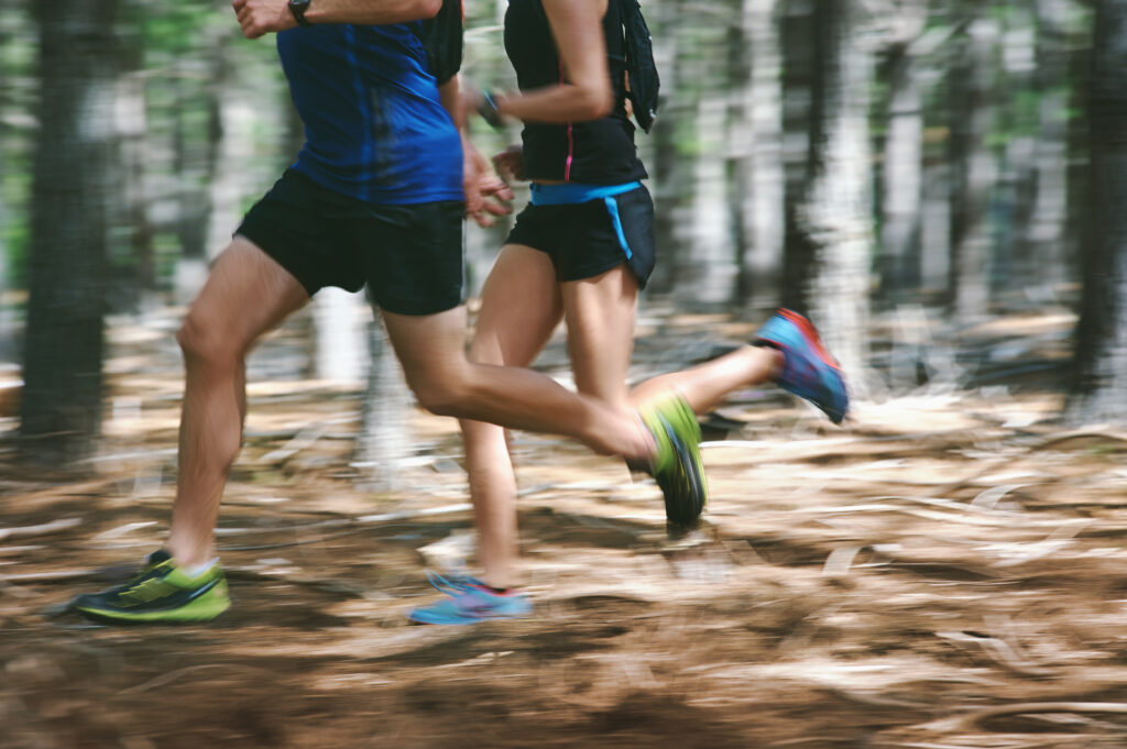 Couple running fast through the forest on trail run 